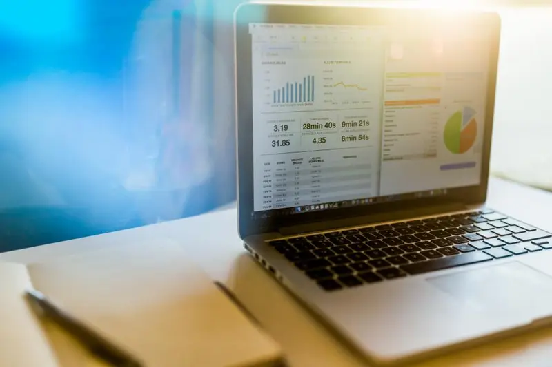 Laptop met financieel dashboard vol grafieken en cijfers naast een notitieboekje op een bureau