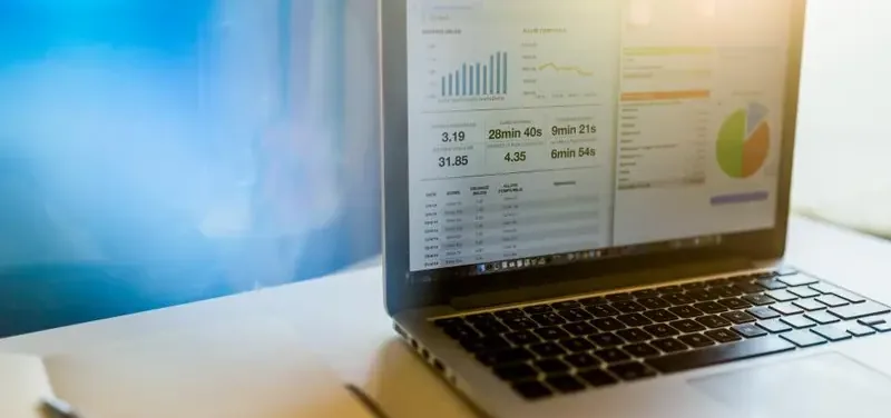 Laptop met financieel dashboard vol grafieken en cijfers naast een notitieboekje op een bureau