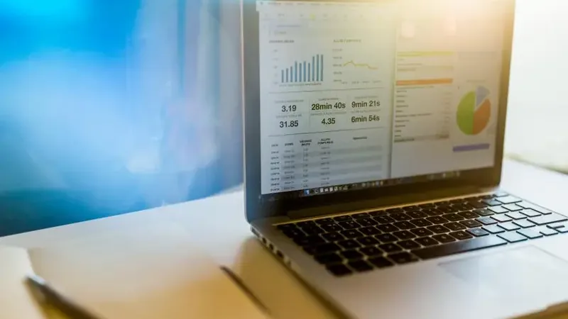 Laptop met financieel dashboard vol grafieken en cijfers naast een notitieboekje op een bureau