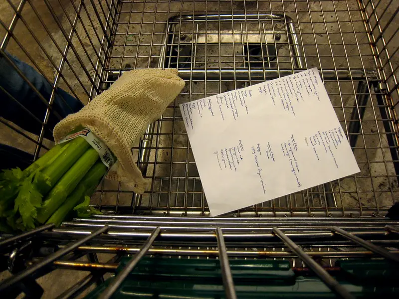 Boodschappenlijstje en verse bleekselderij in een winkelwagentje in de supermarkt