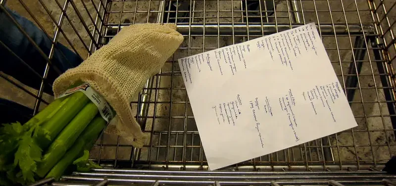 Boodschappenlijstje en verse bleekselderij in een winkelwagentje in de supermarkt