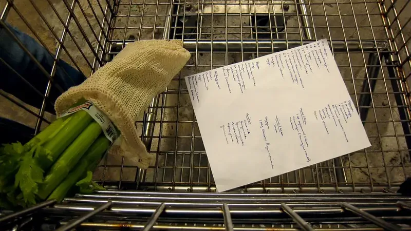 Boodschappenlijstje en verse bleekselderij in een winkelwagentje in de supermarkt
