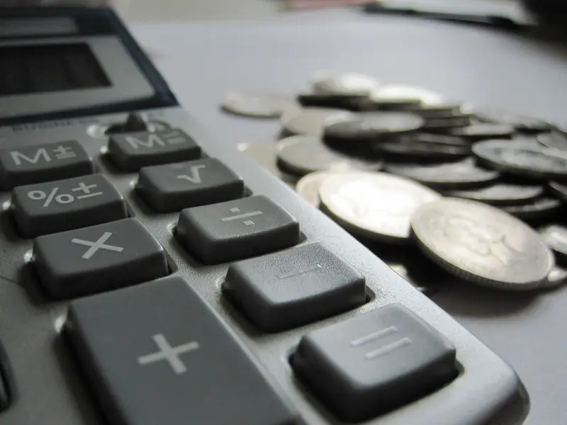 Rekenmachine naast een stapel munten op een bureau, symbool voor persoonlijke financiën