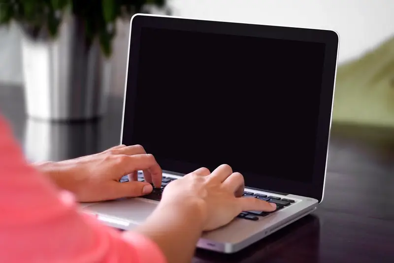 Handen van een zelfstandig ondernemer die aan het typen zijn op een laptop aan een bureau