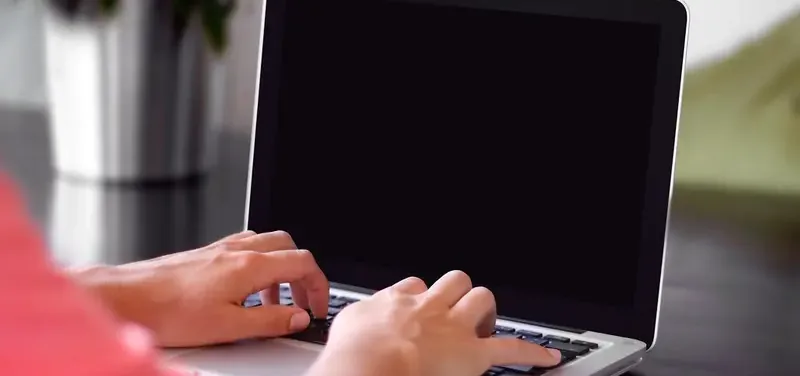 Handen van een zelfstandig ondernemer die aan het typen zijn op een laptop aan een bureau