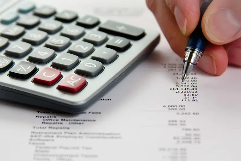 Hand met pen en rekenmachine bij een financieel overzicht