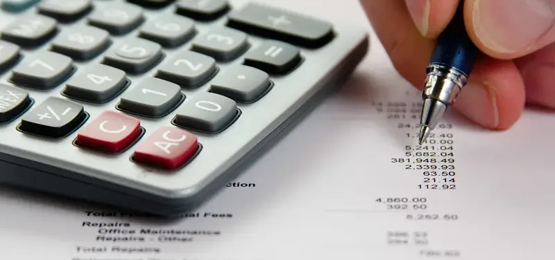 Hand met pen en rekenmachine bij een financieel overzicht