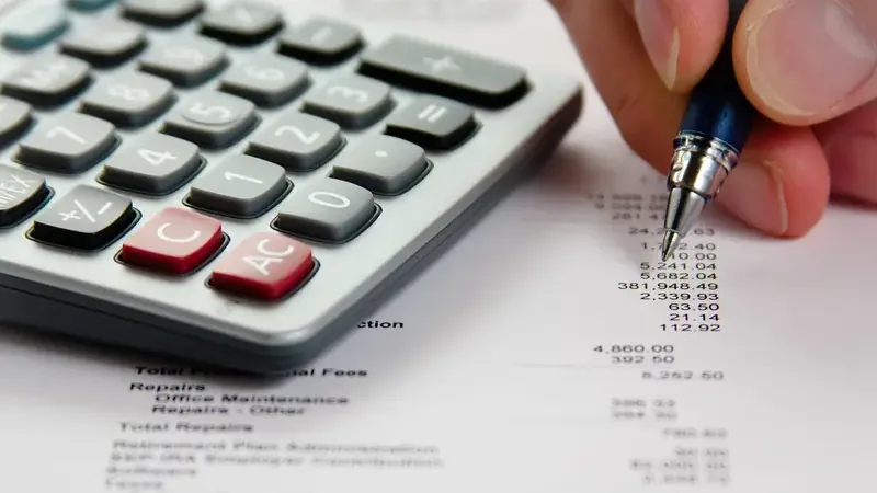 Hand met pen en rekenmachine bij een financieel overzicht